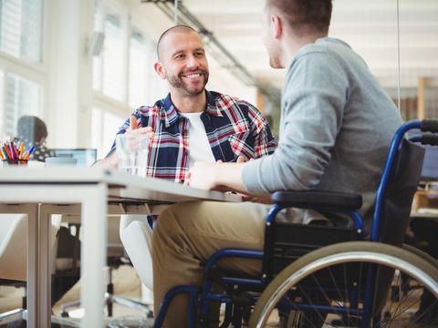 Mann im Rollstuhl im Gespräch mit einem Kollegen im Büro