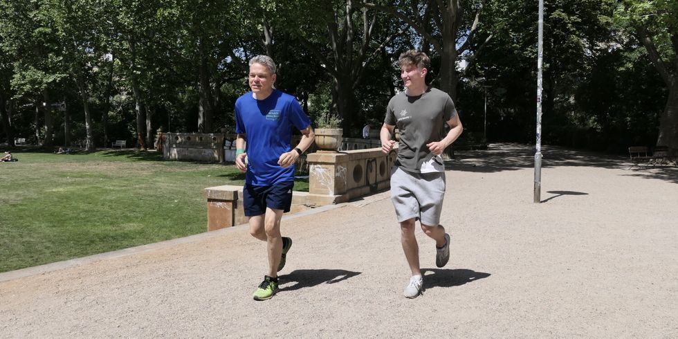 Zwei Männer joggen bei sonnigem Wetter durch einen Park.