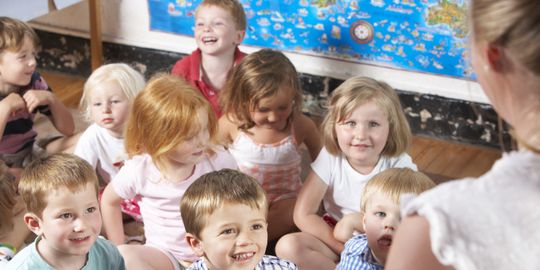 Kinder sitzen im Kindergarten auf dem Boden und hören Erzieherin zu 