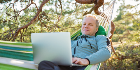 Mann mit einem Laptop in einer Hängematte mitten im Wald