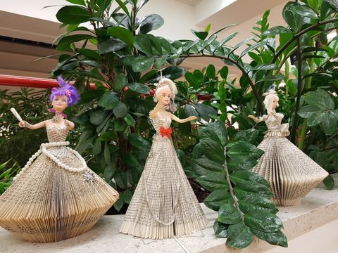 drei Barbiepuppen, bekleidet mit Buchseiten vor einer Grünpflanze