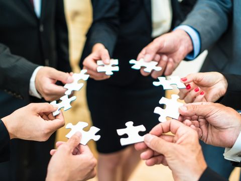 8 Personen halten je ein Puzzle-Stein in der Hand und bilden damit einen Kreis 
