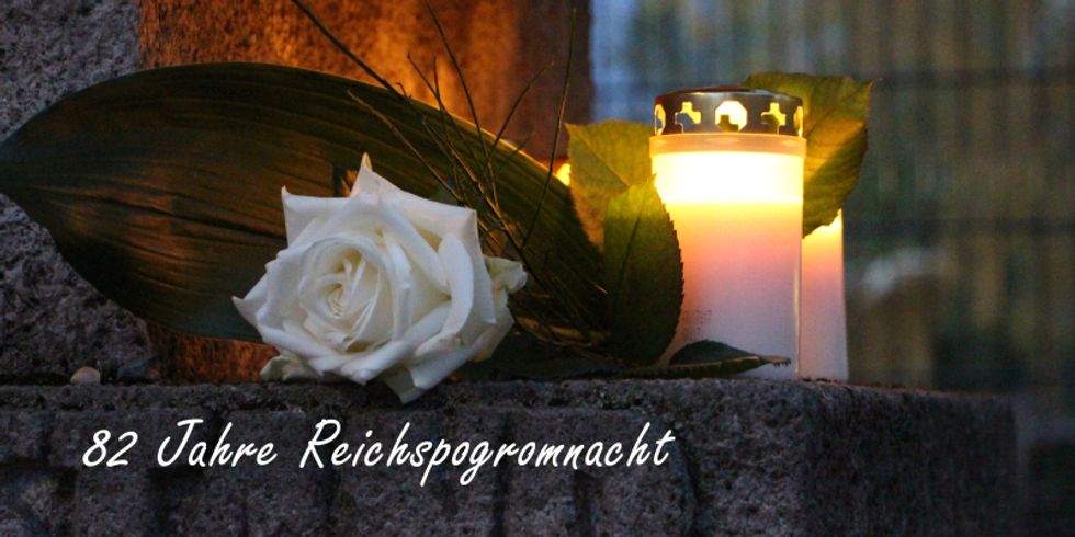 Weiße Rose und Grabkerzen auf einer Steinfläche und dem Schriftzug "82 Jahre Reichspogromnacht"
