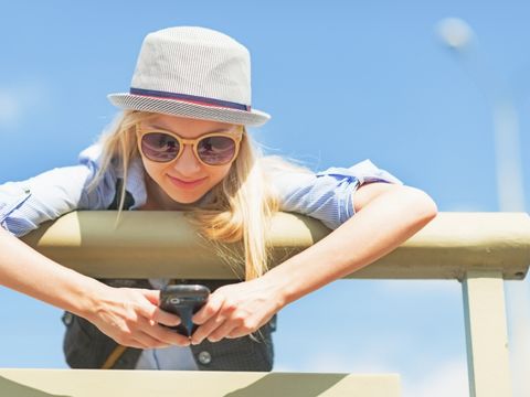 junge Frau mit Hut und Sonnenbrille hält ein Handy