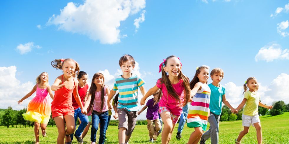 Eine Gruppe von Kinder rennt fröhlich über eine Wiese