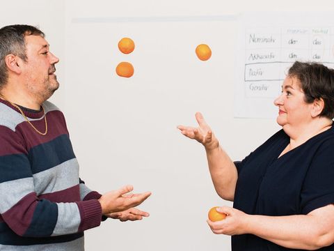 Frau und Mann beim Suppe kochen mit Orangen jonglierend