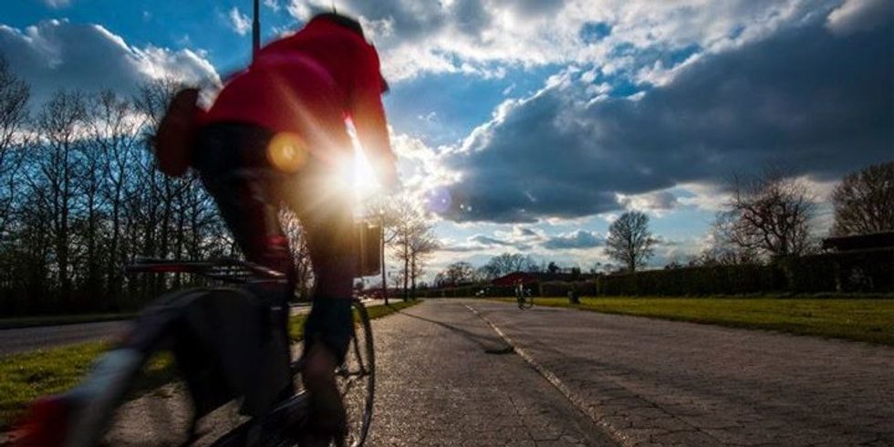 Fahrradfahrende Person fährt auf einer Landstraße in den Sonnenuntergang
