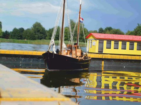 Ein Modellschiff schwimmt auf dem Wasser. Dahinter ist ein kleiner Steg mit einer Miniaturhütte.