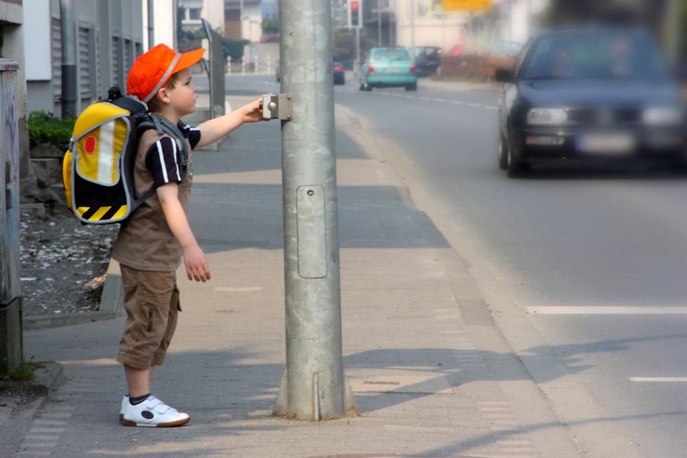 kleiner Schuljunge steht an einer Ampel um die Straße zu überqueren