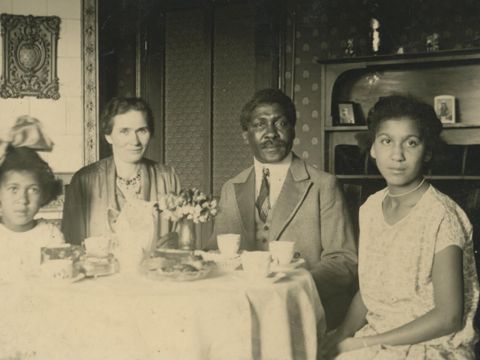 Eine alte Fotografie von einem erwachsenen Paar mit zwei Mädchen an einem Kaffeetisch.