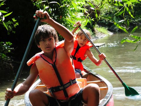 Zwei Jungen mit Schwimmweste fahren Kanu auf einem Fluss