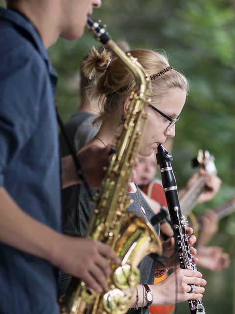 Junge Menschen spielen verschiedene Instrumente, darunter Saxophon, Klarinette und Gitarre