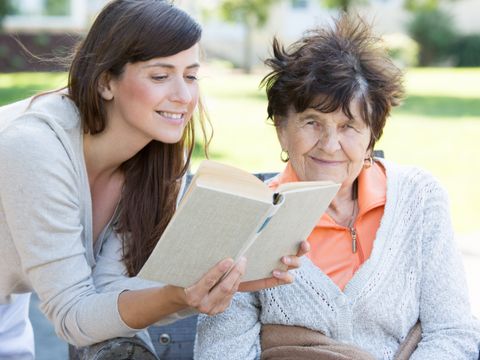 Junge Frau liest Senioren aus einem Buch vor