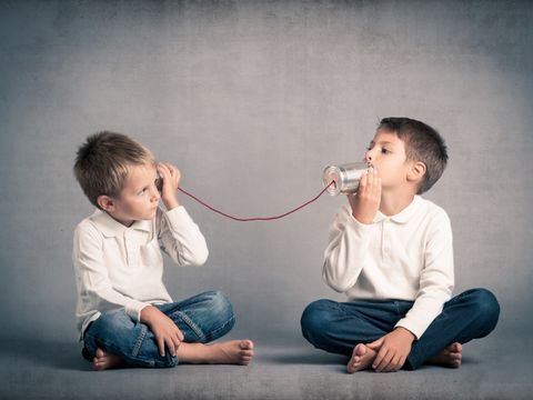 Zwei Jungs telefonieren, indem sie Blechbüchsen an ihre Ohren halten.
