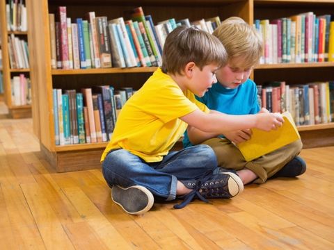 zwei Jungs sitzen vor einem Bücherregal und lesen in einem Buch