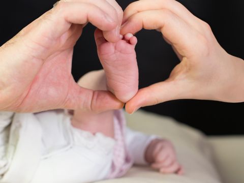 Zwei Hände formen ein Herz um den Fuß eines Säuglings