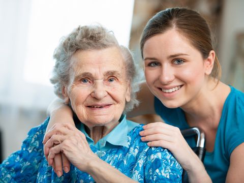 Junge Pflegerin umarmt lächelnde Seniorin