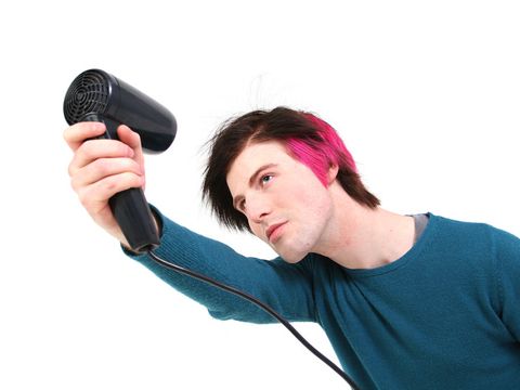 Junger Mann mit teilweise pink gefärbten Haaren fönt sich die Frisur zurecht