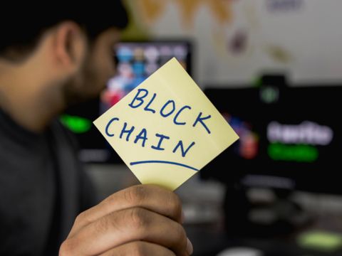 Mann hält Post-it mit dem Wort Blockchain in die Kamera