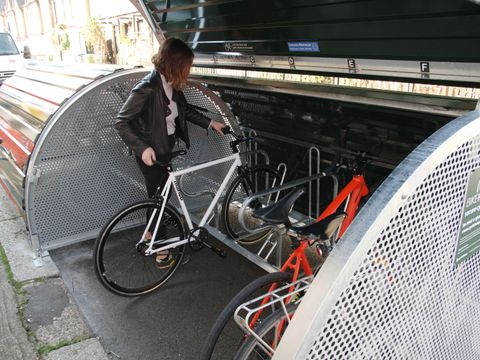 Eine Frau schiebt ein Fahrrad in eine geöffnete Fahrradbox