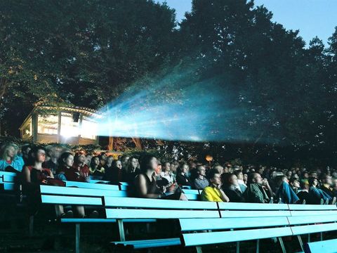 Freiluftkino Hasenheide bei Nacht mit Bäumen im Hintergrund. Der Lichtstrahl des Filmprojektors leuchtet über die Köpfe der Besucher und Besucherinnen