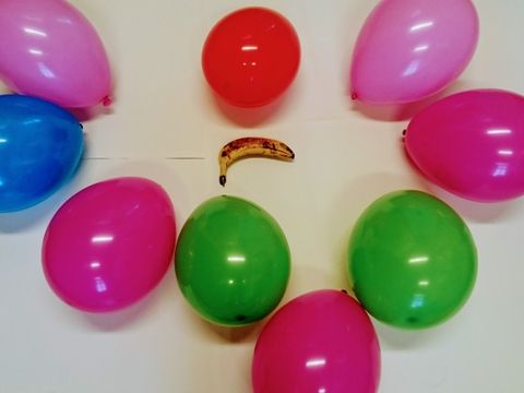 Banane umgeben von 9 bunten Luftballons