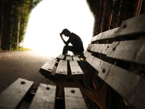 verzweifelter Mann sitzt im Wald auf einer Bank und stützt die Hände in den Kopf