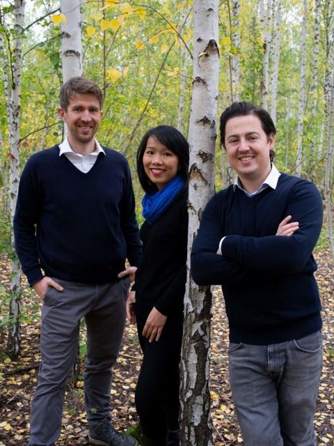 Eine Frau und zwei Männer in einem Wald lachen in die Kamera