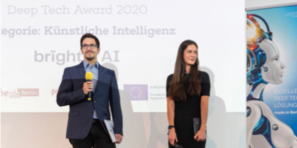 Ein Mann hält ein Mikrofon, daneben steht eine Frau mit einem Award in der Hand