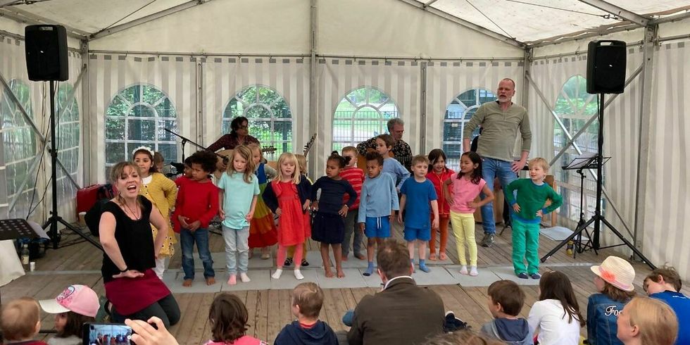 Mehrere Kinder tanzen auf einer kleinen Bühne in einem Zelt. Vor den Kindern hockt eine singenden und tanzende Frau.