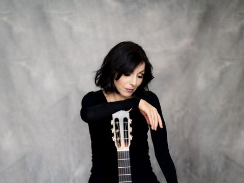 Das Farbporträt zeigt die Gitarristin Sabine Oehring frontal zusammen mit ihrem Instrument.