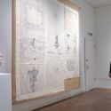 Bildvergrößerung: Ansicht der Galerie, links eine Gipsbüste eines Mannes, in der Mitte ein heller Wandbehang mit Stickerrei und ein Besucher, der diesen betrachtet.