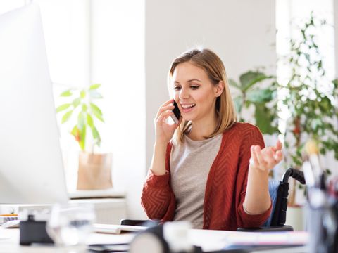 Eine Frau sitzt an einem modernen Arbeitsplatz und telefoniert mit ihrem Mobiltelefon