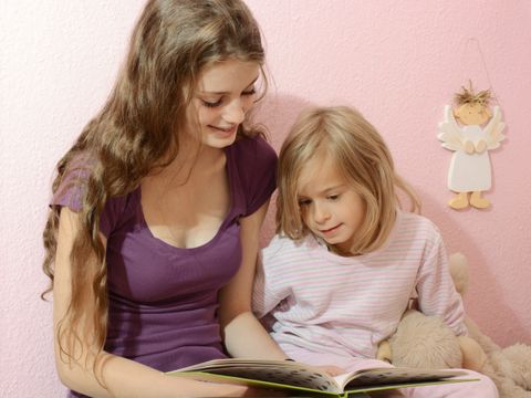 Teenager liest kleinem Mädchen aus Buch vor
