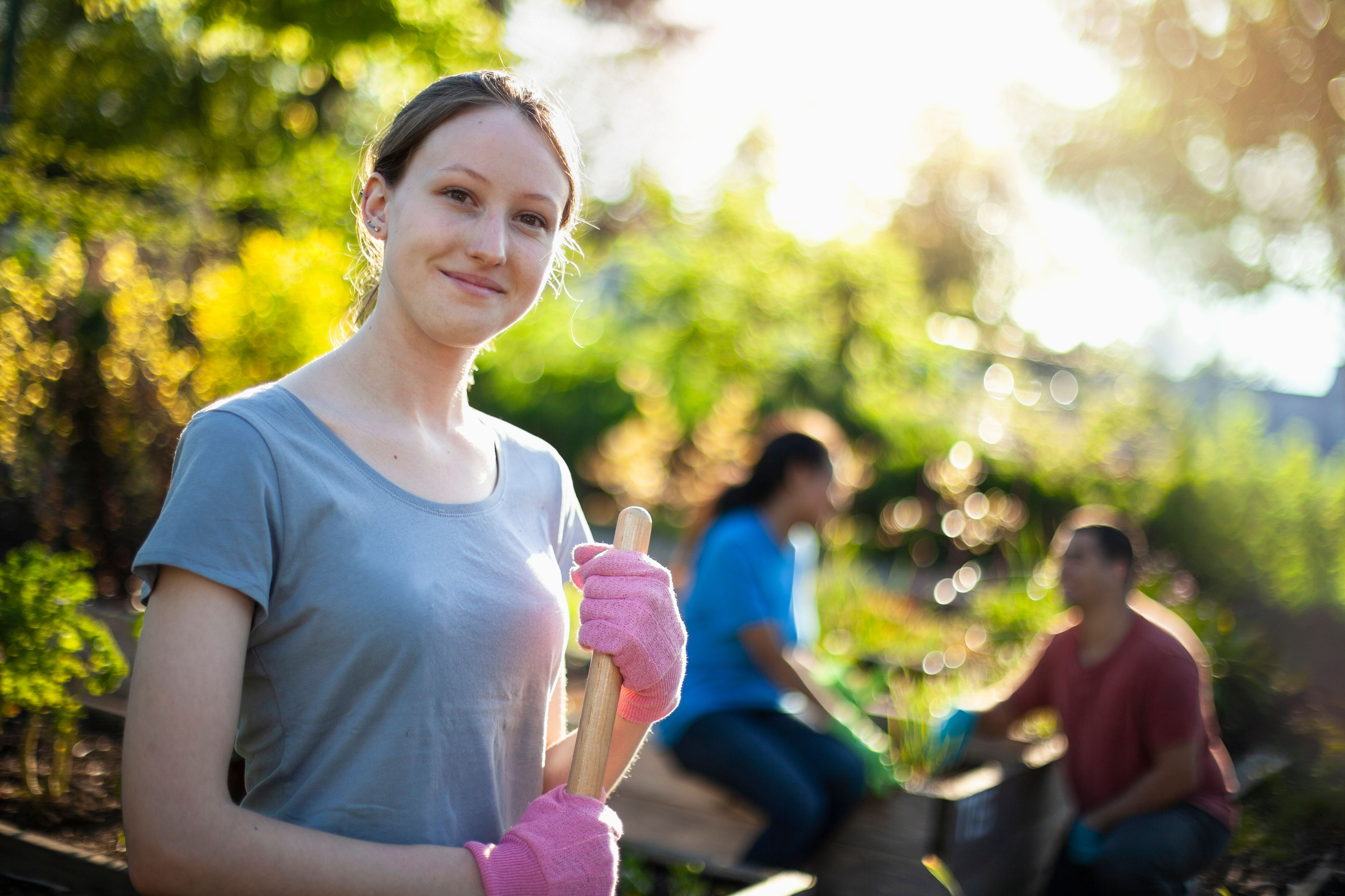 Portrait of Caucasian young woman student working to cleanup community garden neighborhood park area in residential district with youth organization volunteer charity crew in summer