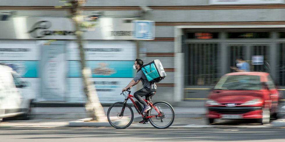 Ein Mitarbeiter eines Lieferdienstes fährt mit dem Fahrrad auf der Straße. 