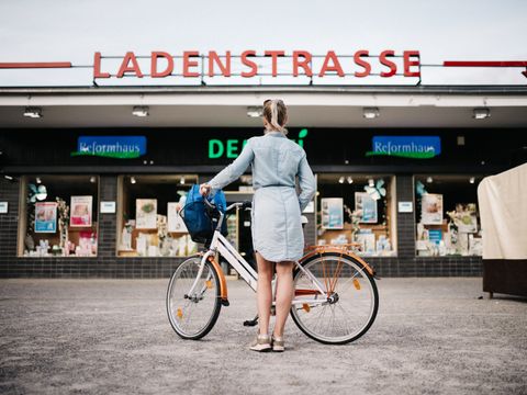 Frau mit Fahrrad vor Ladenstraße