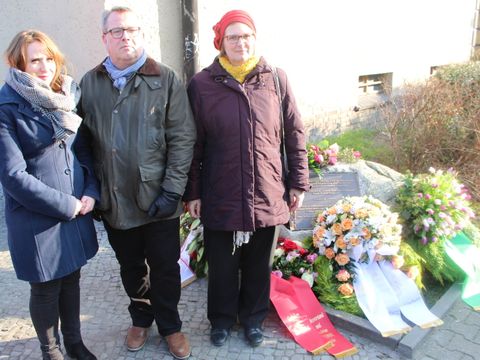 Bildvergrößerung: 2 Frauen und ein Mann stehen an Gedenktafel mit Blumenkränzen.