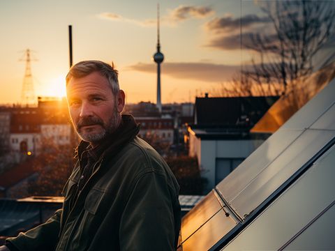 Mann auf Dach neben Solarpanelen, hinter ihm die Stadt Berlin