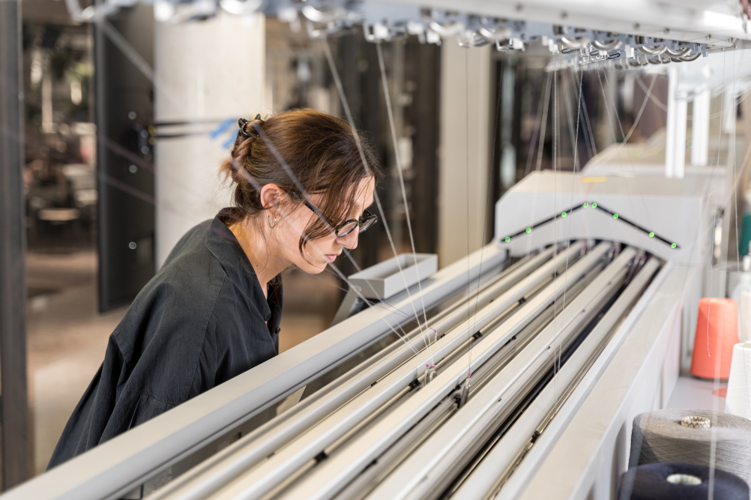 Eine junge Frau steht an einer Maschine die Garne verarbeitet