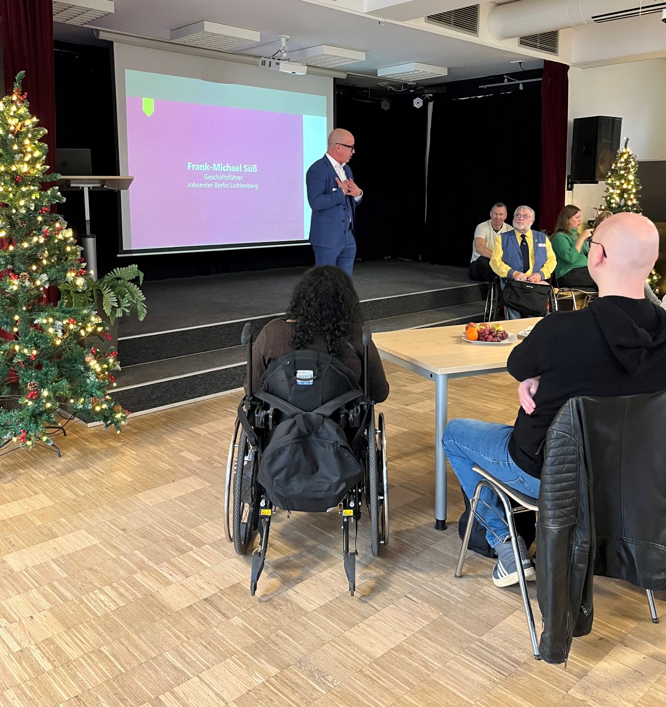 Ein Mann im Anzug spricht zu einer Gruppe von sitzenden Menschen. Eine farbige Präsentation im Hintergrund zeigt seinen Namen: Frank Michael Süß.