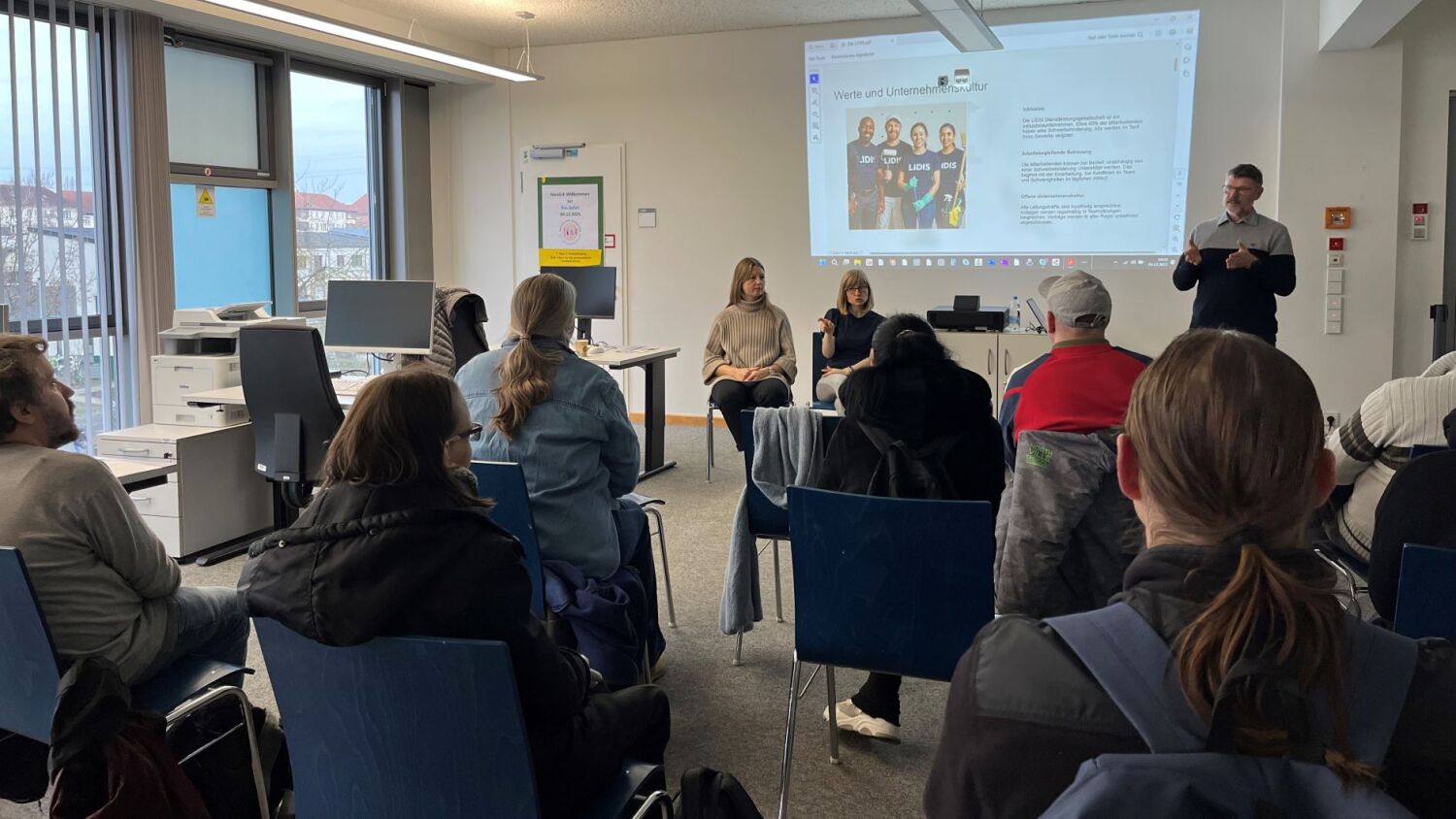 Eine Gruppe von Menschen sitzen in einem Raum und hören dem Vortrag eines Mannes zu.