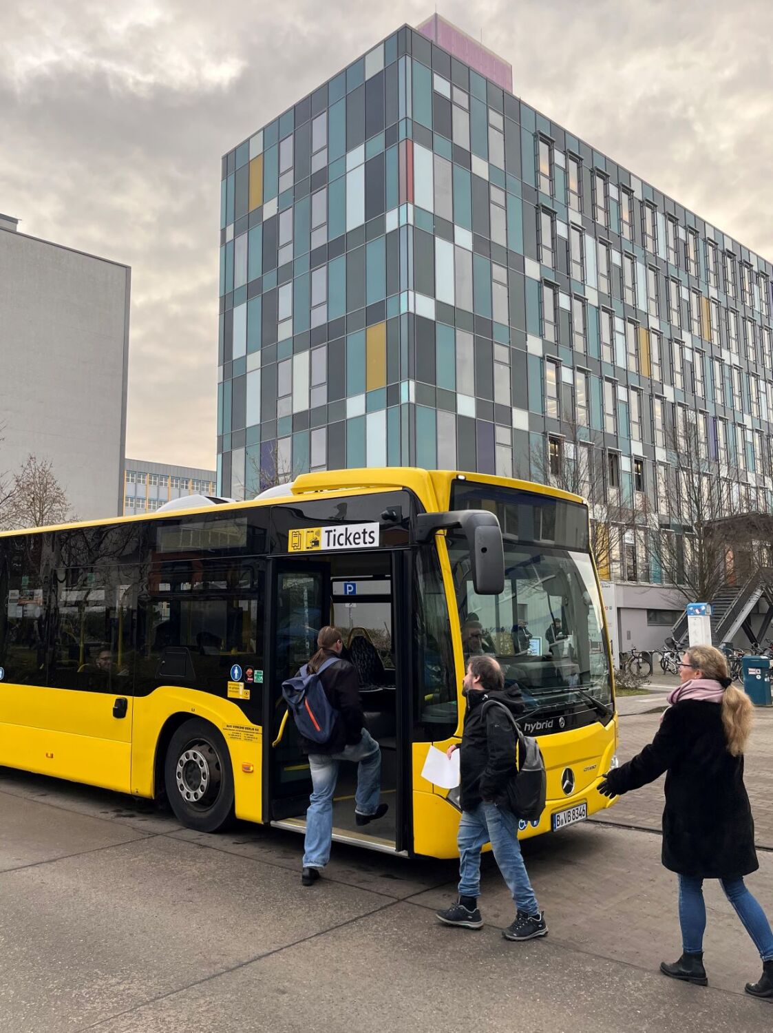 Drei Menschen steigen in einen gelbes Bus ein.