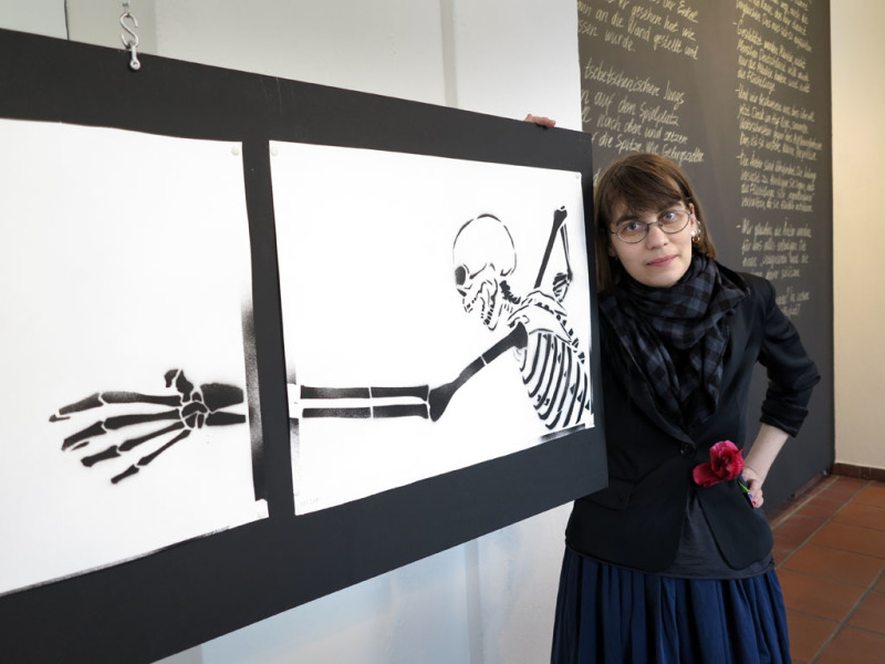Die Künstlerin Nadia Plungian mit ihren Zeichnungen, auf dem ein den Tod darstellendes Skelett mit lang ausholendem Arm gezeichnet ist