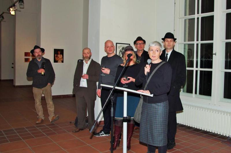 Die Kuratorin Claudia Reinhardt spricht bei der Eröffnung, hinter ihr stehen die Künster*innen der Ausstellung