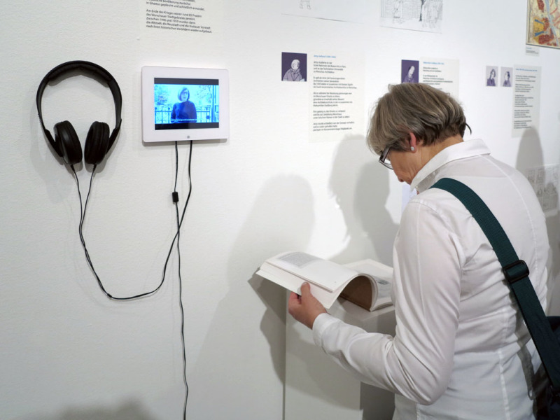 Blick in die Ausstellung mit einer Besucherin, die ein Buch durchblättert
