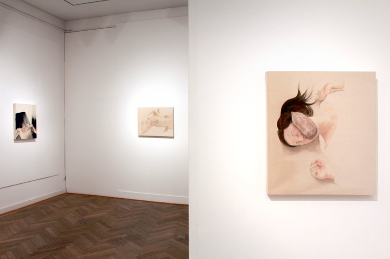 Blick in die Ausstellung, vorn: Malerei vom Gesicht einer Frau auf dem ein (toter) Igel auf dem Rücken liegt