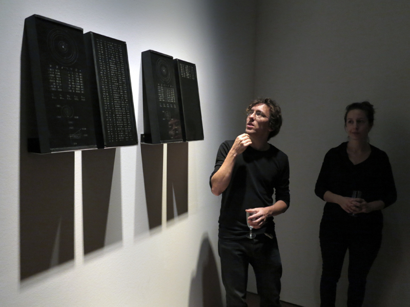 Der Künstler erklärt eine ARbeit, die aus vier schwarzen Granitsteinen auf Regalen besteht