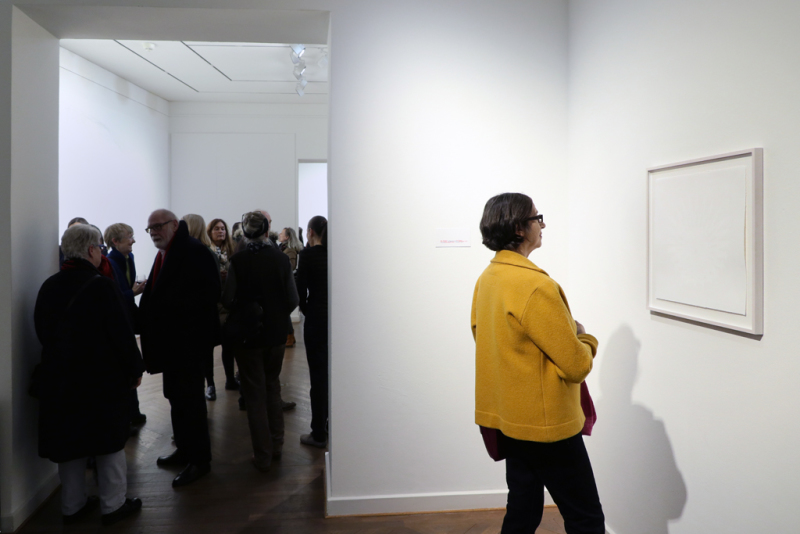 Auf der rechten Seite steht eine Besucherin, welche das Werk "me moved" von Kati Gausman betrachtet. Auf der linken Seite gibt die Fotografie Einsicht in den Ausstellungsraum mit Besuchern.