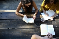 Draufsicht: Drei junge Menschen sitzen an einem Tisch und lesen in Büchern